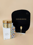 Cosmetic jar with gold lid, black pouch, and decorative spoon on a floral-patterned surface. Cosmetic jar with gold lid, black pouch, and decorative spoon on a floral-patterned surface.