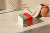 Decorative box with intricate patterns on a light surface with a vase in the background Decorative box with intricate patterns on a light surface with a vase in the background
