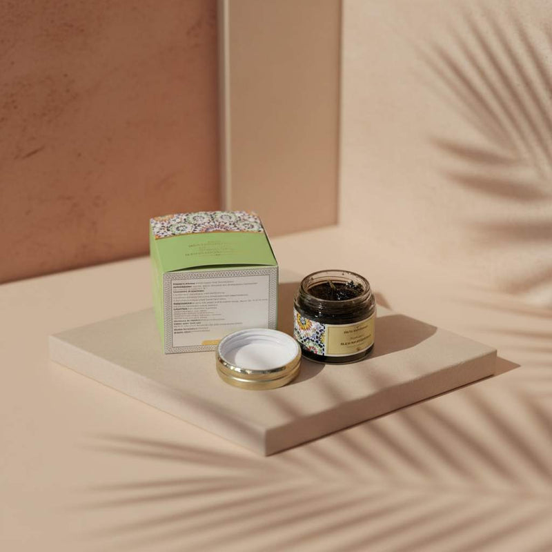 Moroccan black soap in a small jar on a stone plinth, with palm shadows