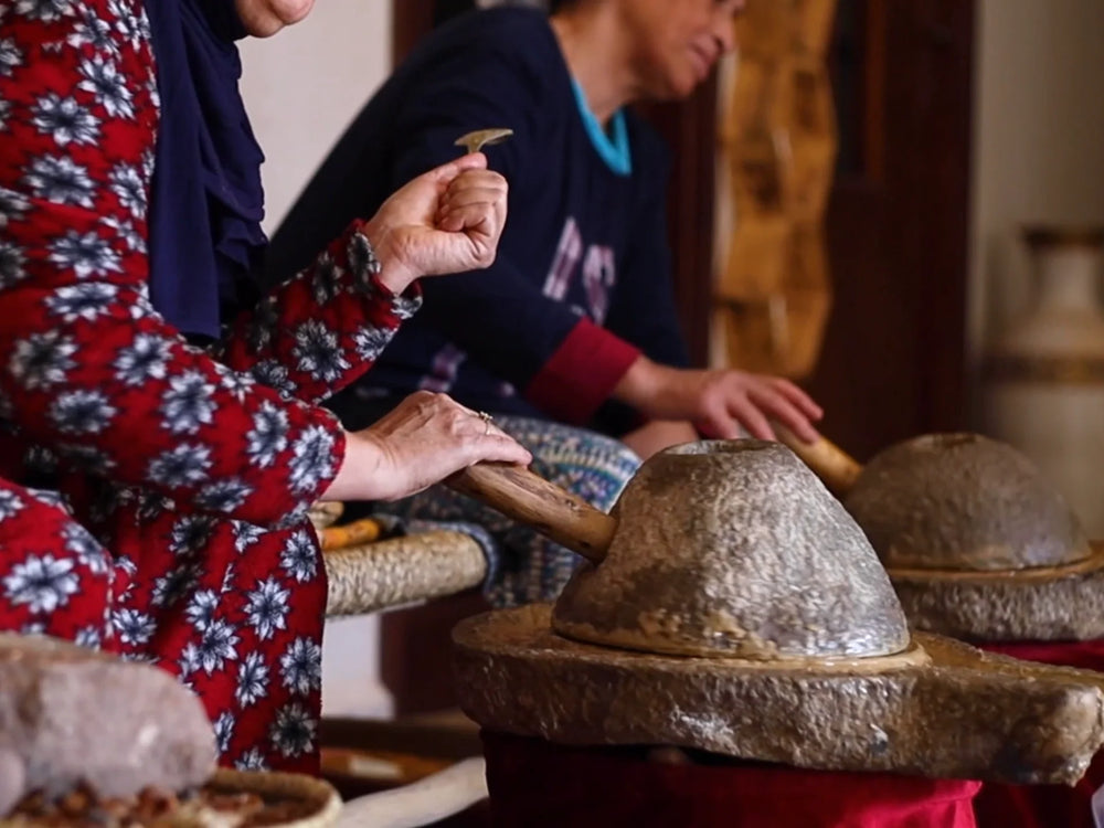 Women cracking argan kernels by hand beside stone argan mills in a cooperative outside Agadir, Morocco
